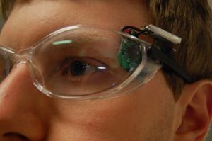 Image: Phillip wearing his wouse prototype, showing the sensor and battery pack attached to the temple of a pair of safety glasses
